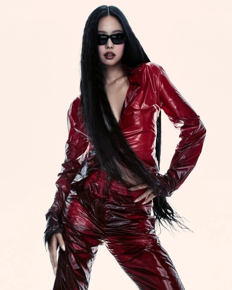 Jennie poses in dark sunglasses and a glossy red outfit against an off-white studio backdrop.