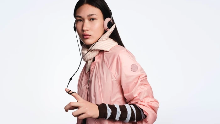 Model Yumi Lambert wearing a pink jacket and headphones against a white background for Moncler Puffy Summer 2026