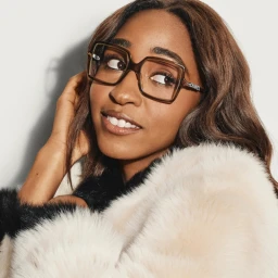Close-up portrait of Ayo Edebiri wearing square glasses and a fluffy white jacket against a neutral studio background.