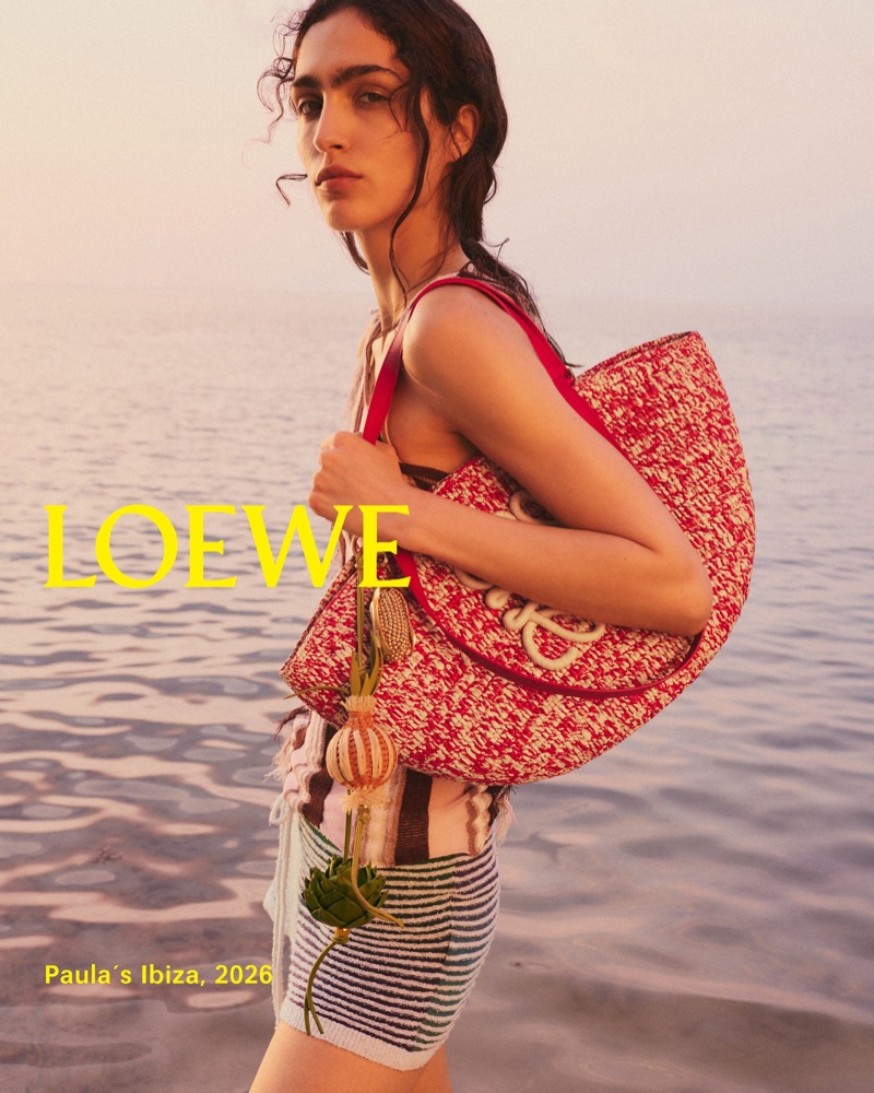 Sara Caballero wearing striped shorts and carrying a red tote bag by Loewe against an ocean backdrop