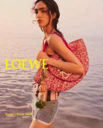 Sara Caballero wearing striped shorts and carrying a red tote bag by Loewe against an ocean backdrop