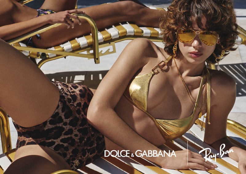 Model reclining on a yellow sun lounger wearing gold aviator sunglasses, metallic bikini top, and leopard print bottoms.