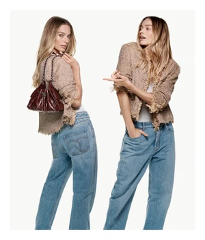Margot Robbie wearing a tweed jacket and blue jeans holding a dark red leather bag against a plain white background