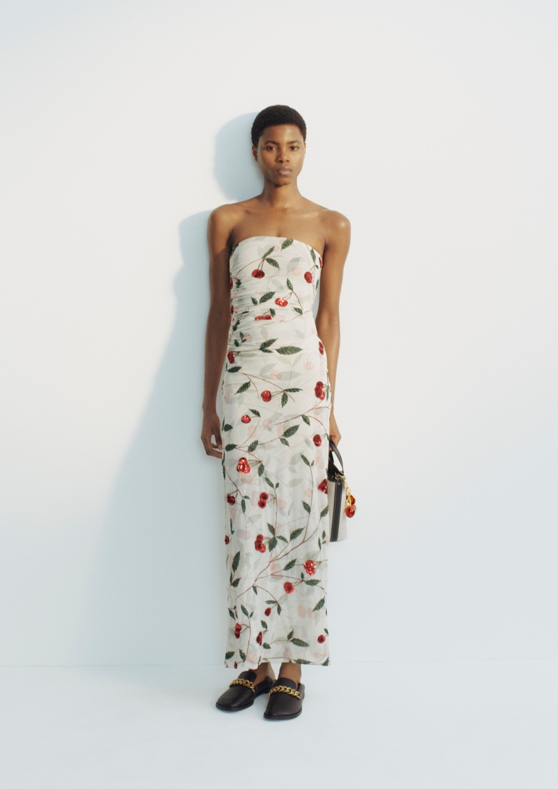 Model wearing a strapless cherry print maxi dress paired with black chain loafers against a clean white backdrop.