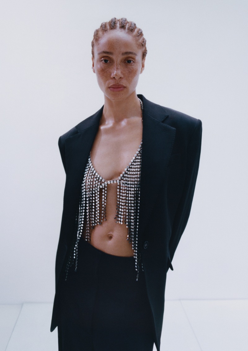 Adwoa Aboah wearing a black tailored blazer over a sparkling crystal fringe top against a white studio background.