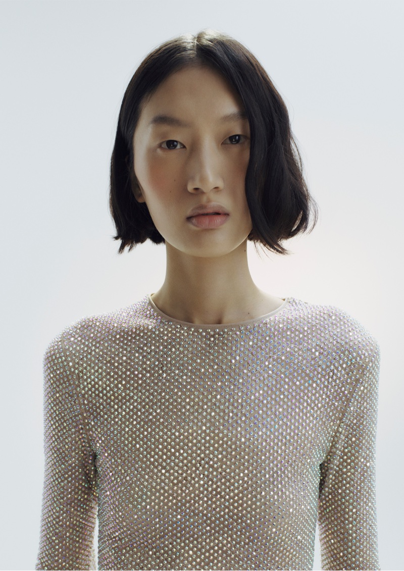 Model Angelina Kendall wearing a sparkling rhinestone mesh top against a soft white studio background.