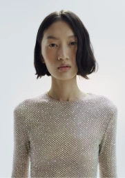 Portrait of an Asian female model wearing a sparkly embellished top against a bright white background