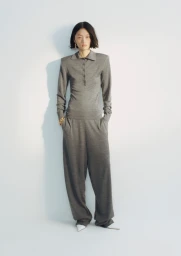 Model wearing a grey polo top and matching trousers standing against a white seamless background.