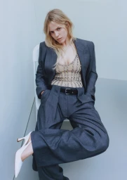 Model seated wearing a grey suit jacket and trousers with a rhinestone embellished corset and white heels