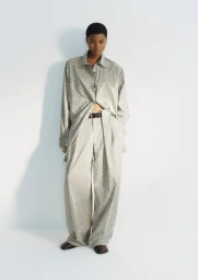Model Adwoa Aboah wearing a shimmering metallic oversized shirt and wide-leg trousers against a plain white studio background