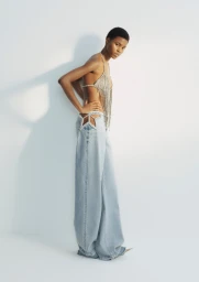 Model Adwoa Aboah wearing a crystal halter top and cutout denim jeans against a white background for H&M