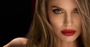Close up beauty portrait of Angelina Jolie wearing bold red lipstick and dark eyeliner against a dark background.