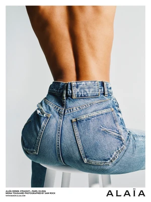 Model Mona Tougaard wearing blue denim jeans, seated on a white stool against a light background for Alaïa Denim Debut Campaign.