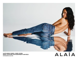 Mona Tougaard lying on a reflective white surface wearing denim jeans for the Alaïa Denim Debut Campaign