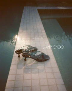 Jimmy Choo heeled sandals resting on a tiled pool edge at dusk by Henrik Purienne