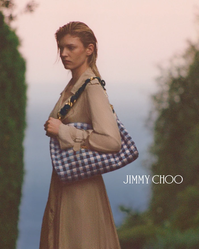 Model Camille Chifflot holding a blue and white plaid shoulder bag outdoors in a portrait by Henrik Purienne for Jimmy Choo.