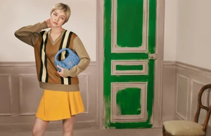 Gigi Hadid wearing a brown striped sweater and yellow skirt holding a blue leather handbag