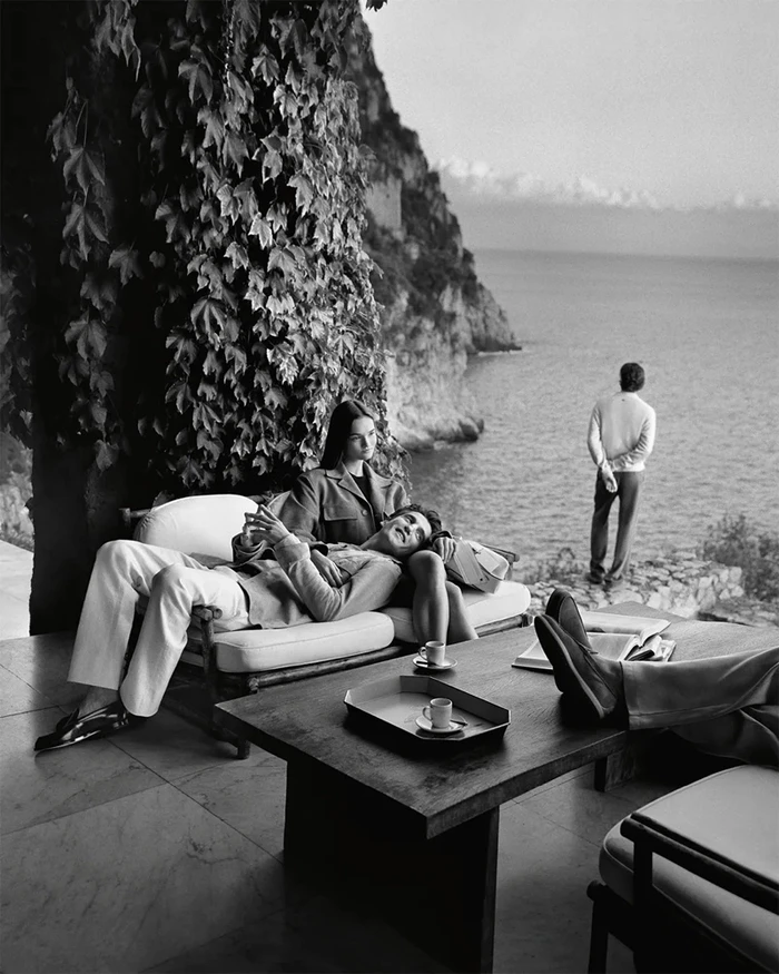 Black and white editorial image of models relaxing on a terrace overlooking the sea for Tod's Italian Stories campaign.