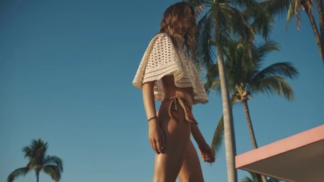 Model wearing a cream crochet cape top and bikini bottoms against palm trees and a clear blue sky for Zimmermann Summer Swim 2026
