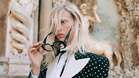 Model Vilma Friedlander holding black geometric sunglasses wearing a polka dot jacket outdoors