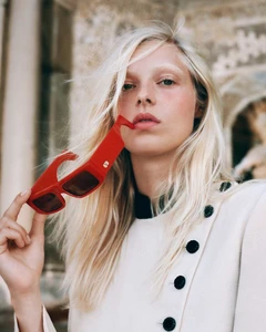 Model Vilma Friedlander holding red sunglasses near her mouth, wearing a white buttoned coat for Valentino