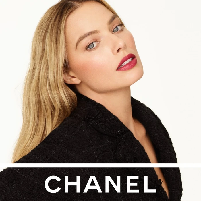 Margot Robbie wearing a black tweed jacket with bold pink lipstick for Chanel Rouge Allure Velvet campaign against a white backdrop