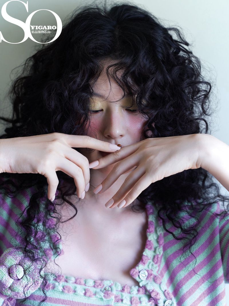 Portrait of an adult woman with curly black hair, light skin, and a pastel-colored sweater, posing for a fashion magazine cover.