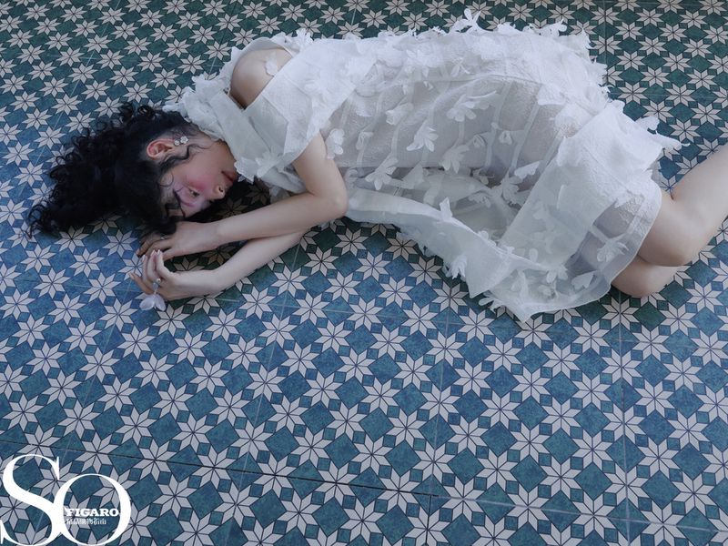 Young woman in a white dress lies on a patterned tile floor, a high-angle view capturing her relaxed pose and the intricate dress details.