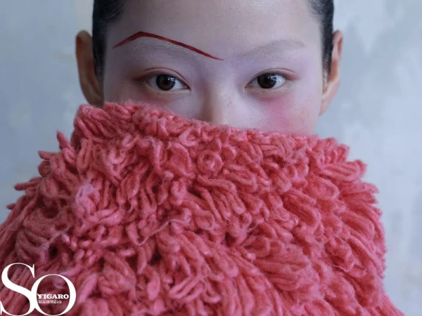 Close-up shot of a woman with creative makeup, including a drawn-on eyebrow, covering her face with a fluffy, textured garment.