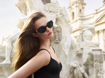 Model Lulu Tenney wearing black sunglasses and a black top outdoors in front of a classical stone fountain monument.