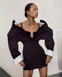 Model in black structured dress with oversized white cuffs and crystal earrings against a plain white wall