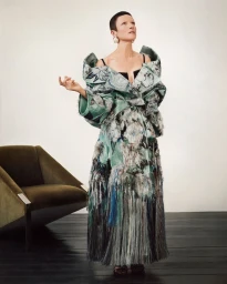 Model standing in a structured green patterned coat with oversized shoulders, wearing earrings and dark dress