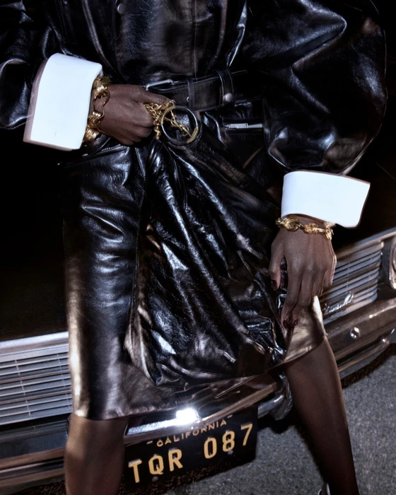 Model in shiny black leather coat leaning against a vintage car with California license plate