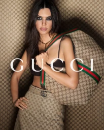 Emily Ratajkowski wearing monogrammed skirt and holding a large Gucci handbag against monogrammed background