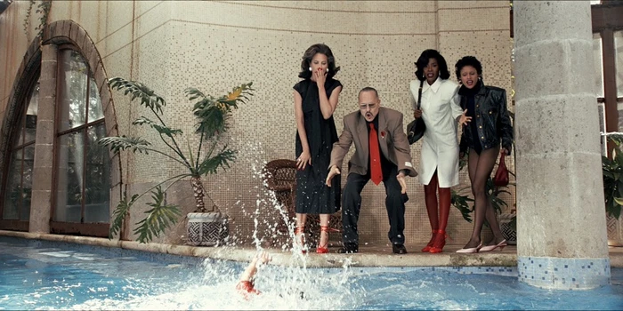 Four people standing shocked by a swimming pool watching someone splash in the water for Zara Vatísimo