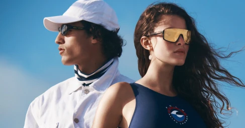 Man in white baseball cap and sunglasses standing next to a woman in a blue tank top against a clear sky background