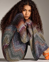 Model with long curly dark hair wearing a patterned knit chevron dress in a studio setting.