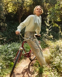 Steffi Cook in pale blouse and distressed denim posing with a red bicycle on a woodland path for Kenzo Spring Flowers