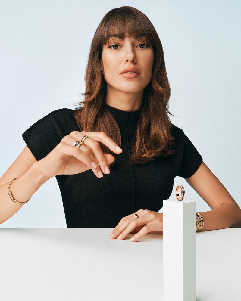 Dilan Çiçek Deniz posing in a black top with Boucheron Quatre rings and bracelets behind a white table.