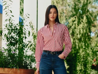 Model Jade Nguyen in a red and white striped long-sleeve shirt and blue jeans standing outdoors near foliage.