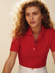 Model with curly blonde hair wearing a red polo shirt against a light background for Tommy Hilfiger