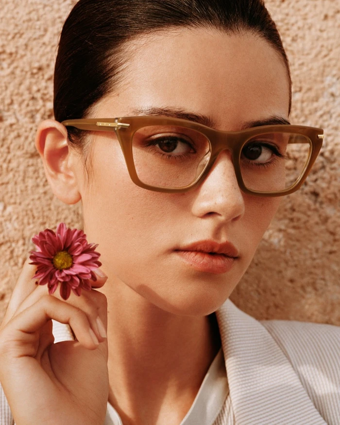 Close-up portrait of a woman wearing tortoiseshell glasses and holding a pink flower for Emporio Armani