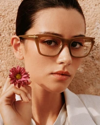 Close-up portrait of a woman wearing tortoiseshell glasses and holding a pink flower for Emporio Armani