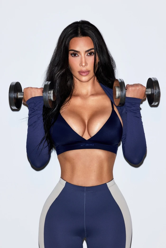 Kim Kardashian lifting dumbbells wearing a blue sports bra and high waisted leggings