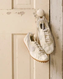 White Nike Moon Shoe sneakers hanging by their laces from a white round door knob on a distressed cream wooden door.