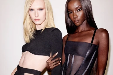 Alex Consani and Anok Yai posing together in black fashion wear against a neutral background for Revolve Los Angeles.