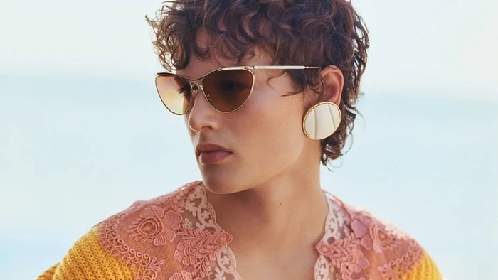Model wearing gold cat-eye sunglasses and large circular earrings with an openwork lace top for Chloe