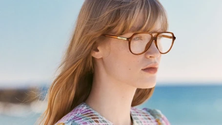 Model wearing brown aviator eyeglasses and a patterned top against an ocean horizon background for Chloé eyewear campaign