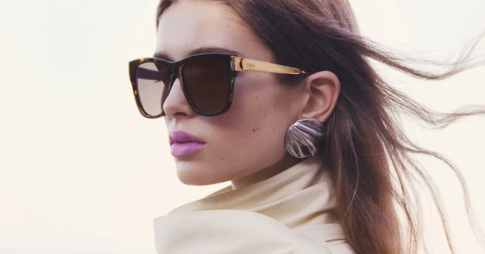 Model wearing tortoiseshell sunglasses and a large silver earring with long brown hair blowing in the wind for Chloé.