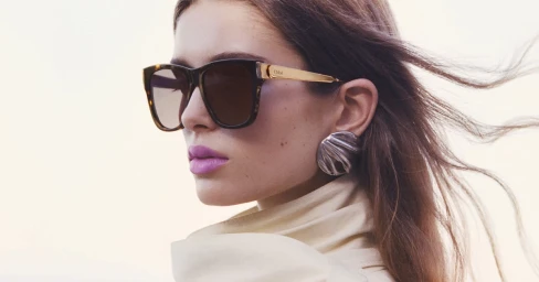 Model wearing tortoiseshell sunglasses and a large silver earring with long brown hair blowing in the wind for Chloé.